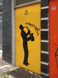 872063 Afbeelding van een deur met een schildering van een saxofonist, naast de ingang van het voormalige jazzpodium ...